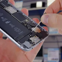 Dłoń wyciąga taśmę z wnętrza otwartego telefonu, odsłaniając baterię.